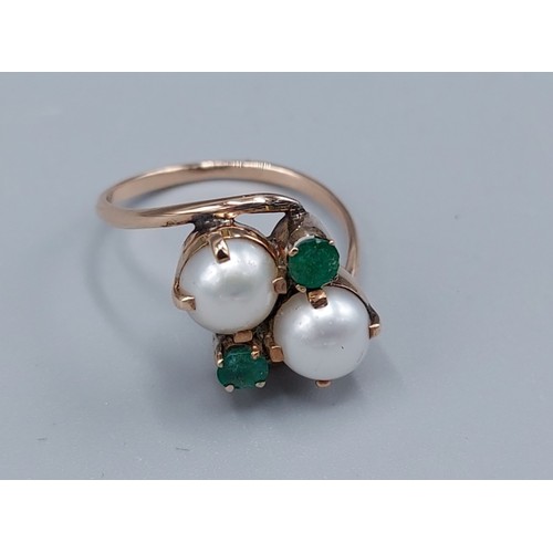 115 - An unmarked tested gold cross-over ring set with two Pearls and two Emeralds, claw set, 2.8gms, ring... 