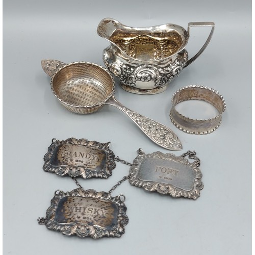 187 - A silver cream jug together with three London silver decanter labels, a London silver tea strainer a... 