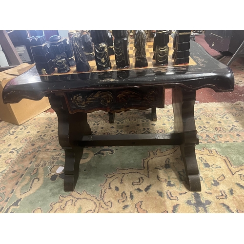 305 - Bespoke carved chess table with 2 matching folding chairs together with carved chess pieces in drawe... 