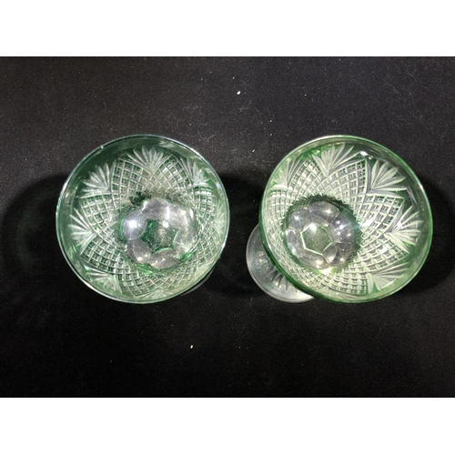 246 - Stevens and Williams - a pair of green overlay wine glasses, the bowls cut through to colourless gla... 