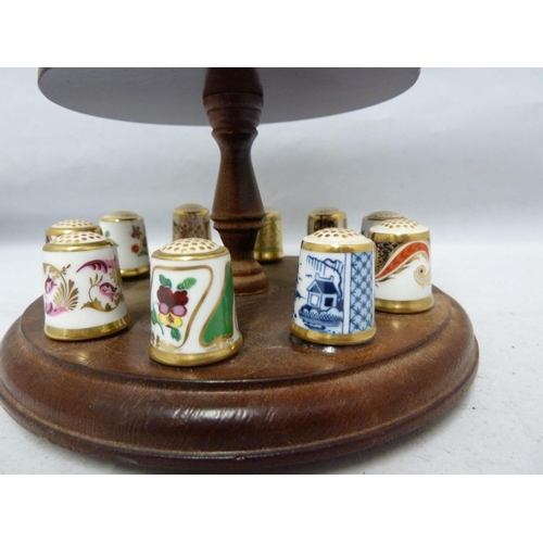 110 - Royal Crown Derby - a collectors full set of 15 porcelain thimbles on a wooden stand with pin cushio... 