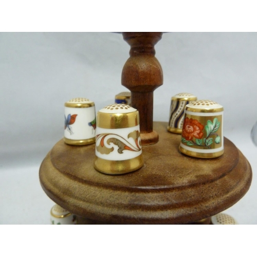 110 - Royal Crown Derby - a collectors full set of 15 porcelain thimbles on a wooden stand with pin cushio... 