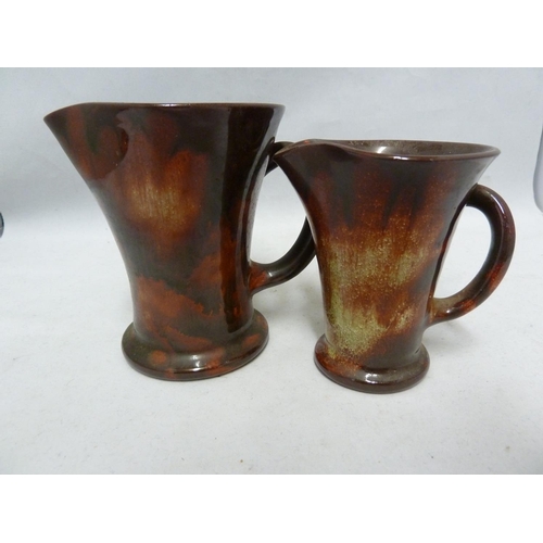 130 - Ewenny Pottery - a milk and cream jug set, the flared cylindrical bodies glazed in a spattered treac... 