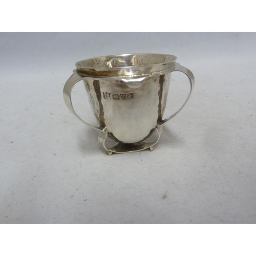 7 - An Arts and Crafts silver egg cup, the plannished body applied with three barbed handles forming a t... 