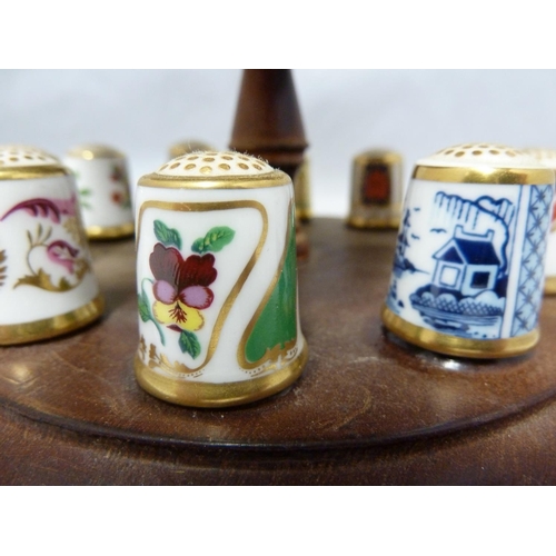 110 - Royal Crown Derby - a collectors full set of 15 porcelain thimbles on a wooden stand with pin cushio... 