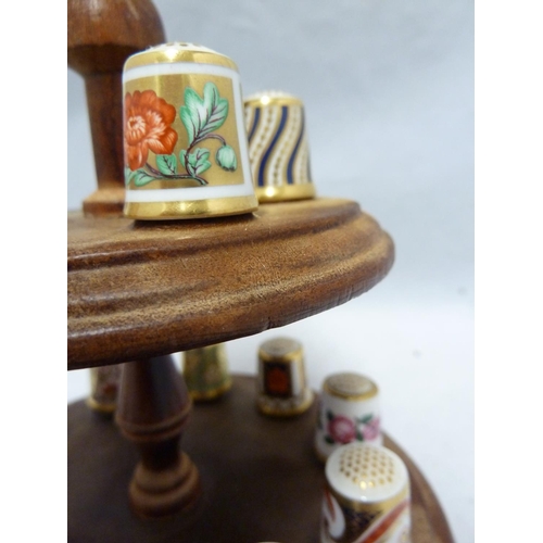 110 - Royal Crown Derby - a collectors full set of 15 porcelain thimbles on a wooden stand with pin cushio... 