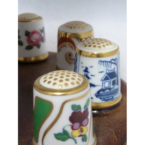 110 - Royal Crown Derby - a collectors full set of 15 porcelain thimbles on a wooden stand with pin cushio... 