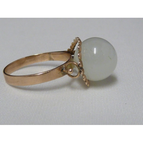 70 - A Chinese white jade ring, the ball form stone set in wirework and on a yellow metal shank stamped K... 