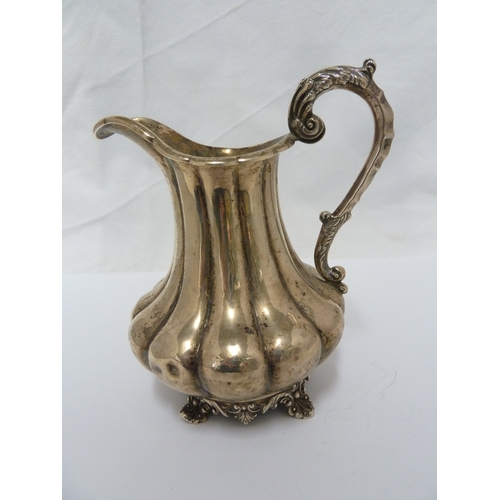 16 - A silver jug, the body of lobed squat baluster form with high foliate scroll handle and upon four vo... 