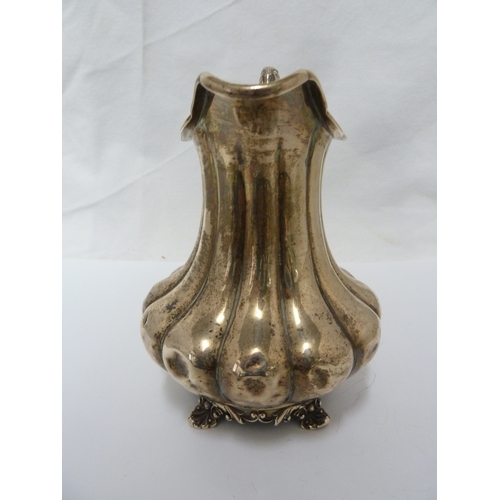 16 - A silver jug, the body of lobed squat baluster form with high foliate scroll handle and upon four vo... 