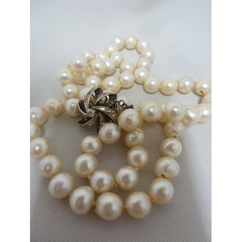 23 - A string of 58 baroque pearls, the diamond set clasp of floret form stamped 14 K, 63.2 grms total we... 