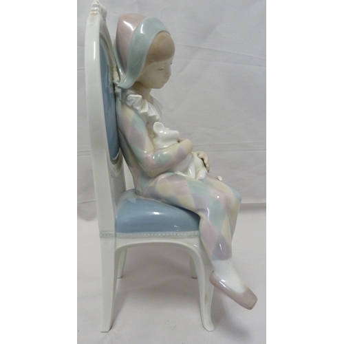 62 - A Lladro figure of the boy harlequin seated in a balloon back chair and holding a white cat, his cos... 