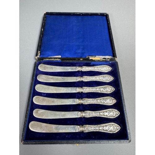 35 - Cased set of six ornate silver‑handled table knives, fitted case — 149g.

Heavily embossed silver ha... 