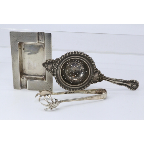 23 - Silver hallmarked sugar tongs, engine turned ashtray, silver tea strainer approx.130g