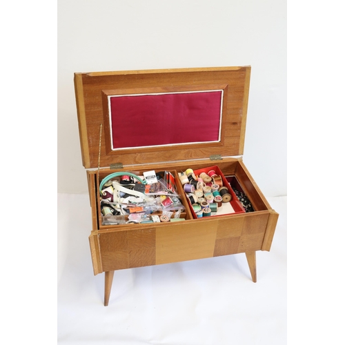 94 - A vintage teak sewing box on raised legs stained to top with contents