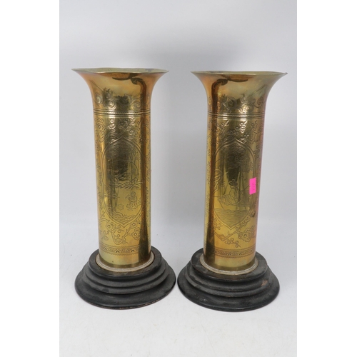 484 - A pair of heavily engraved brass trench art  vases on wooden plinth bases