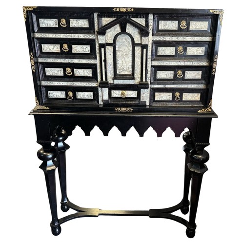 An Italian ebonised and ivory inlaid cabinet, 17th century, on later stand, with gilt metal mounts and handles, the central door opening to reveal six mirrored panels and a shelf, above a single drawer flanked by a further eight drawers, the ebonised stand probably 19th century, with turned tapering supports joined by a stretcher, decorated with total height 135cm, width 95cm, depth 31cm.
