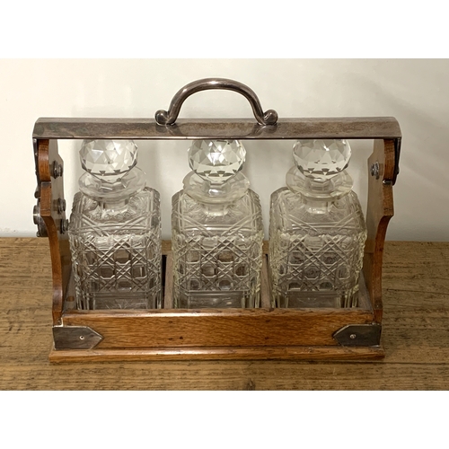 230 - Betjemanns patent oak framed three bottle tantalus with white metal mounts (some chipping to neck of... 