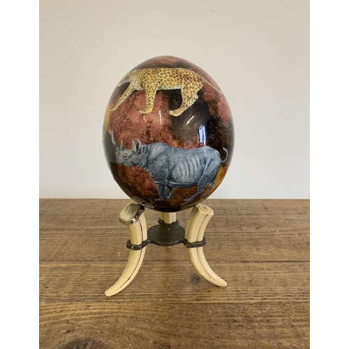 283 - A decoupage ostrich egg decorated with African animals on a faux tusk stand, 9 1/4