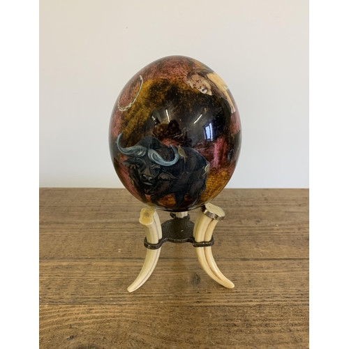 283 - A decoupage ostrich egg decorated with African animals on a faux tusk stand, 9 1/4