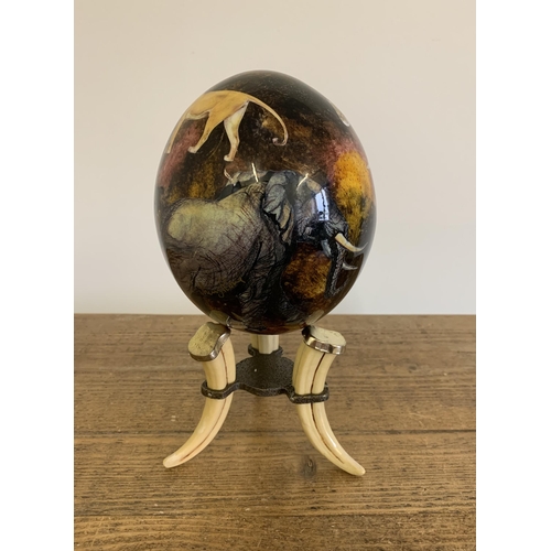 283 - A decoupage ostrich egg decorated with African animals on a faux tusk stand, 9 1/4