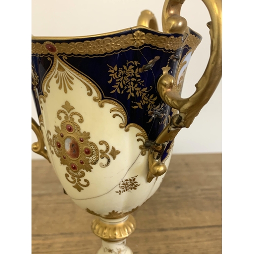 251 - A 19th Century ornate Coalport hand painted three handled cup decorated with a panel of a building o... 