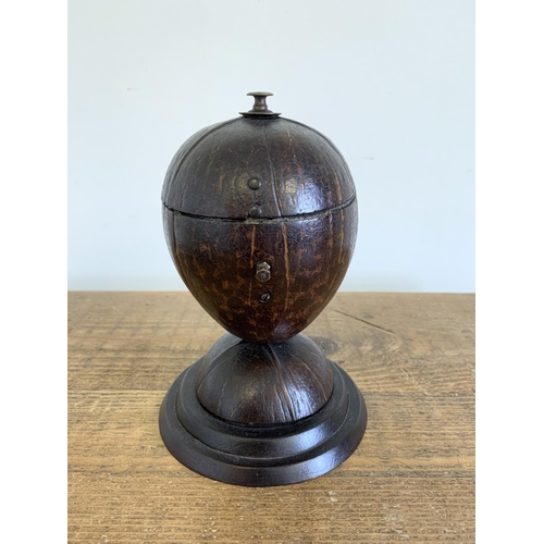 148 - A vintage coconut tobacco holder constructed from a coconut shell hinged in the middle of a wood bas... 