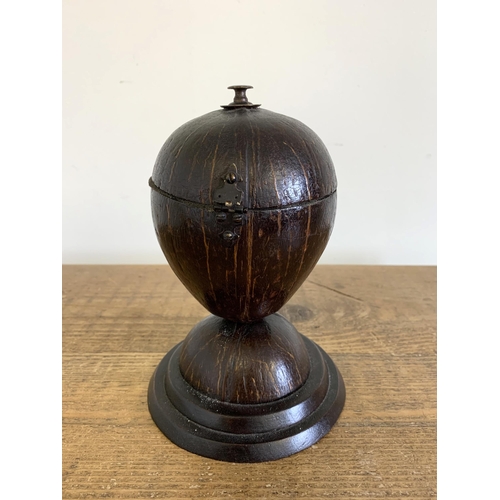 148 - A vintage coconut tobacco holder constructed from a coconut shell hinged in the middle of a wood bas... 