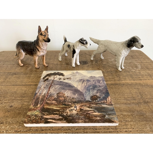 218 - A hand painted glazed tile plus three dog figurines including a Royal Doulton German Shepherd (hairl... 