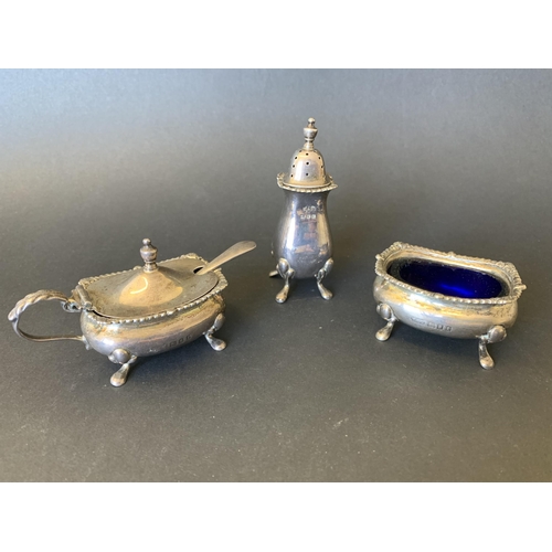 102 - A three piece hallmarked silver condiment set including open salt with blue glass liner, pepper and ... 