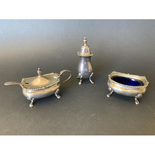 102 - A three piece hallmarked silver condiment set including open salt with blue glass liner, pepper and ... 