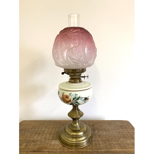 96 - A Victorian brass base oil lamp with hand painted reserve and ornate cranberry to clear glass shade,... 