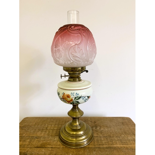 96 - A Victorian brass base oil lamp with hand painted reserve and ornate cranberry to clear glass shade,... 