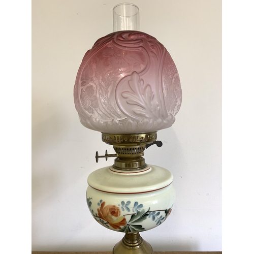 96 - A Victorian brass base oil lamp with hand painted reserve and ornate cranberry to clear glass shade,... 