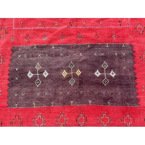 437 - A red ground patterned floor rug with tassels to one end, approx. 8 ft x 13 ft (wear in places)