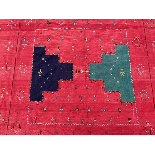 437 - A red ground patterned floor rug with tassels to one end, approx. 8 ft x 13 ft (wear in places)