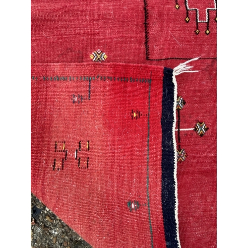 437 - A red ground patterned floor rug with tassels to one end, approx. 8 ft x 13 ft (wear in places)