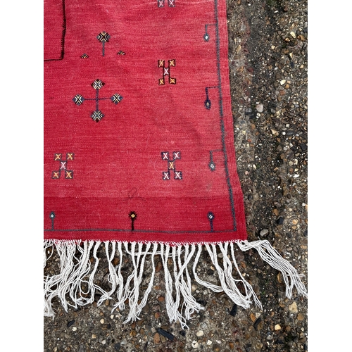 437 - A red ground patterned floor rug with tassels to one end, approx. 8 ft x 13 ft (wear in places)