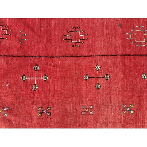 437 - A red ground patterned floor rug with tassels to one end, approx. 8 ft x 13 ft (wear in places)