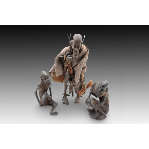 436 - An African Tribal Wood Carving of an Elder with a Leather Bag on his Back + 2 Sitting People.

Heigh... 