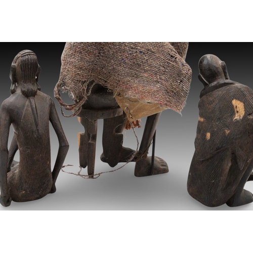 436 - An African Tribal Wood Carving of an Elder with a Leather Bag on his Back + 2 Sitting People.

Heigh... 