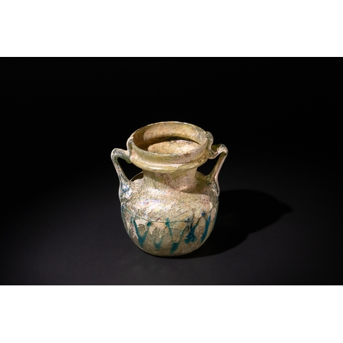 105 - A Roman Beige & Blue Glass Twin Handled Jar, 3rd–4th century A.D., Decorated with Zigzag Patterns.

... 