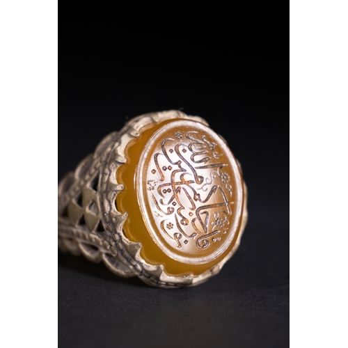 52 - An Islamic Silver Ring with Inscribed Honey Agate.

A silver ring featuring an openwork triangular b... 