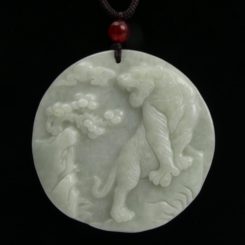 110 - Chinese celadon carved jade pendant with a tiger design on cord, 50mm in diameter.