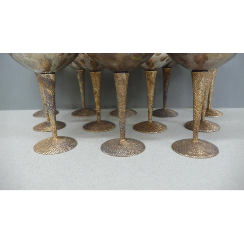 64 - A set of twelve Stuart Devlin parcel Gilt silver cocktail goblets with hammered bowls, twist bark de... 