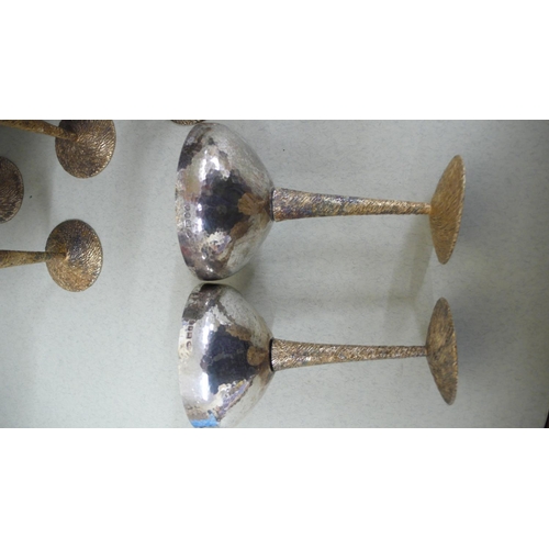 64 - A set of twelve Stuart Devlin parcel Gilt silver cocktail goblets with hammered bowls, twist bark de... 