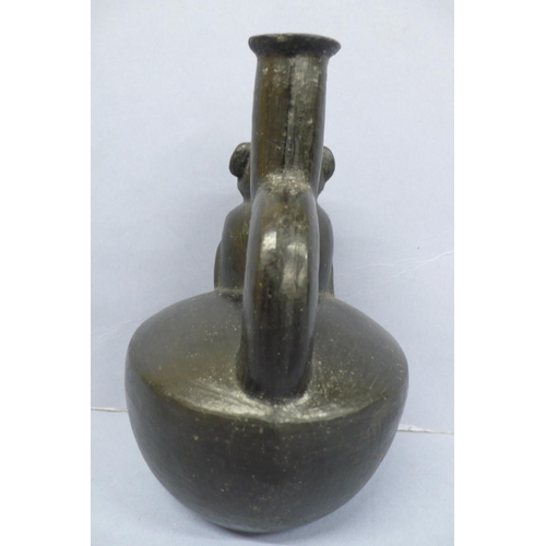 134 - A Vicus Blackware Pottery Effigy Stirrup Handle Vessel in the form of a restrained man in a conical ... 