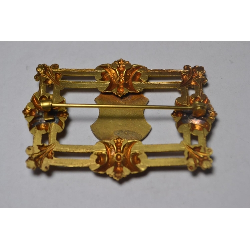 120 - Gold plated brooch having enamelled shield centre in a scrolling frame