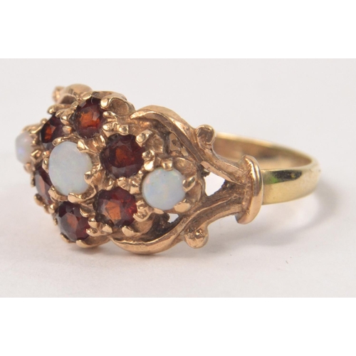 58 - 9ct Opal and garnet set ring. 3 Opals circled by 6 garnets in a floral design. Size N