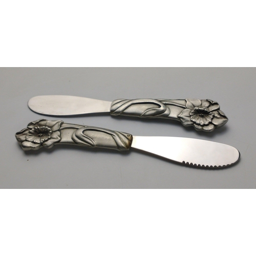 94 - A boxed set of four butter knives with a daffodil pattern on the handle, possibly pewter, by AMERICA... 